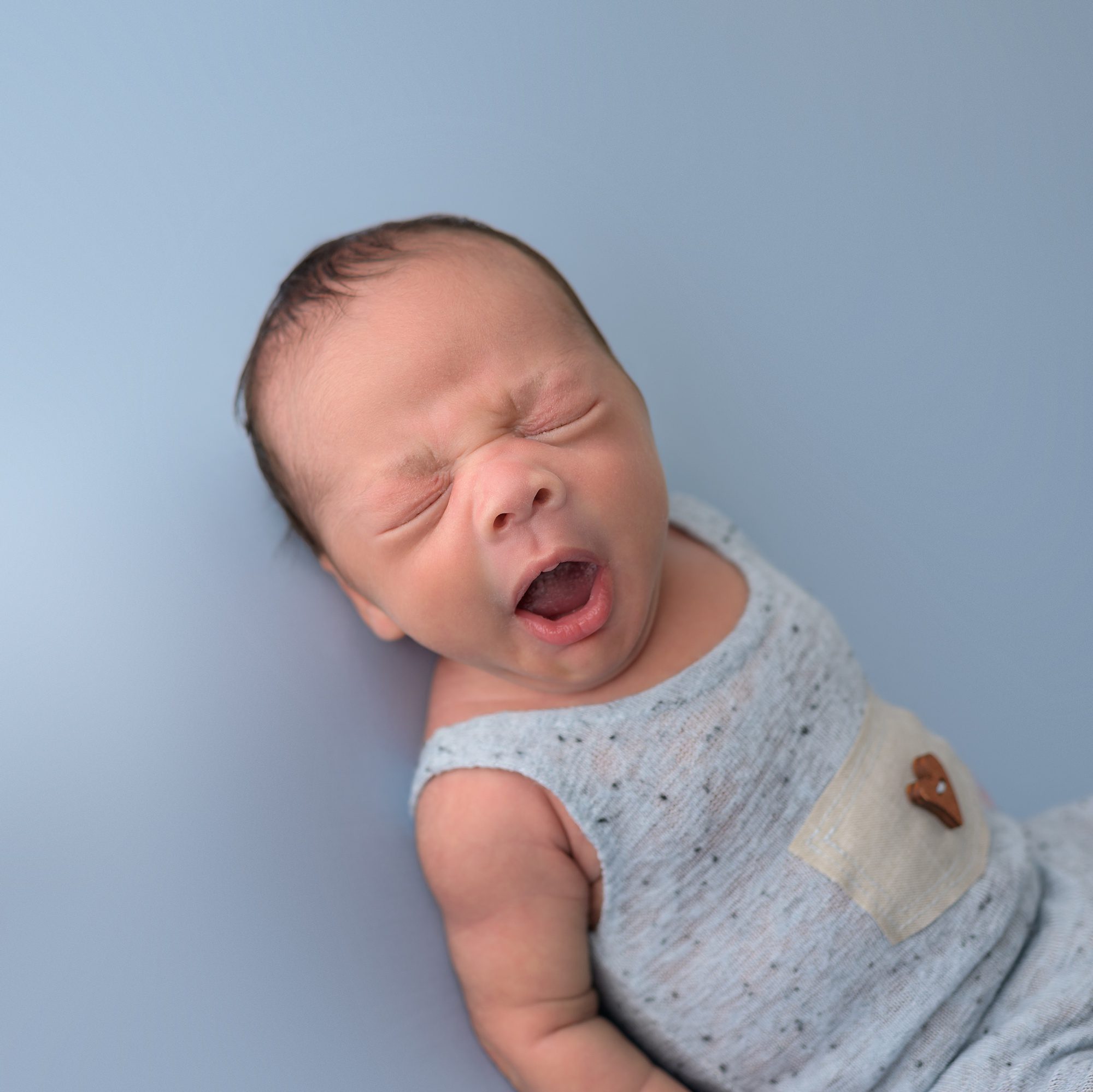 Yawning baby boy on blue backdrop, photographed by one of the best baby photographers in Kansas City Helen Ransom.