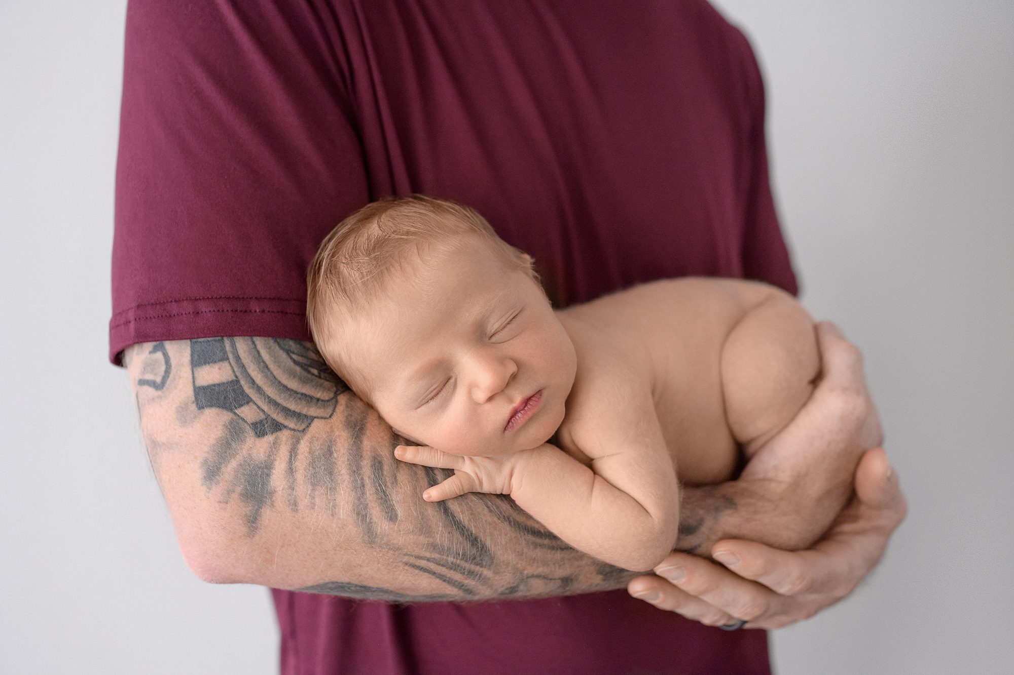 Newborn baby laying across dad's arm, which showcases his tattoos.