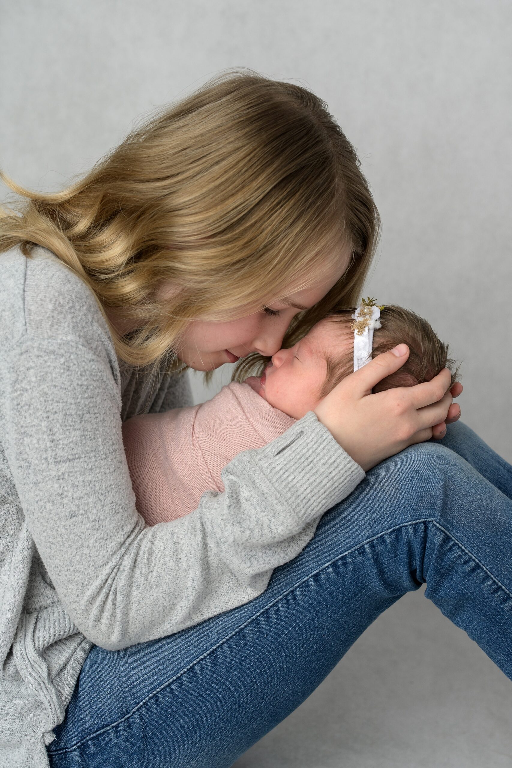 Two sisters, one newborn and one elementary school aged. The older sister has her nose and forehead touching to the nose and forehead of the baby, taken by Kansas City newborn photography studio Helen Ransom.