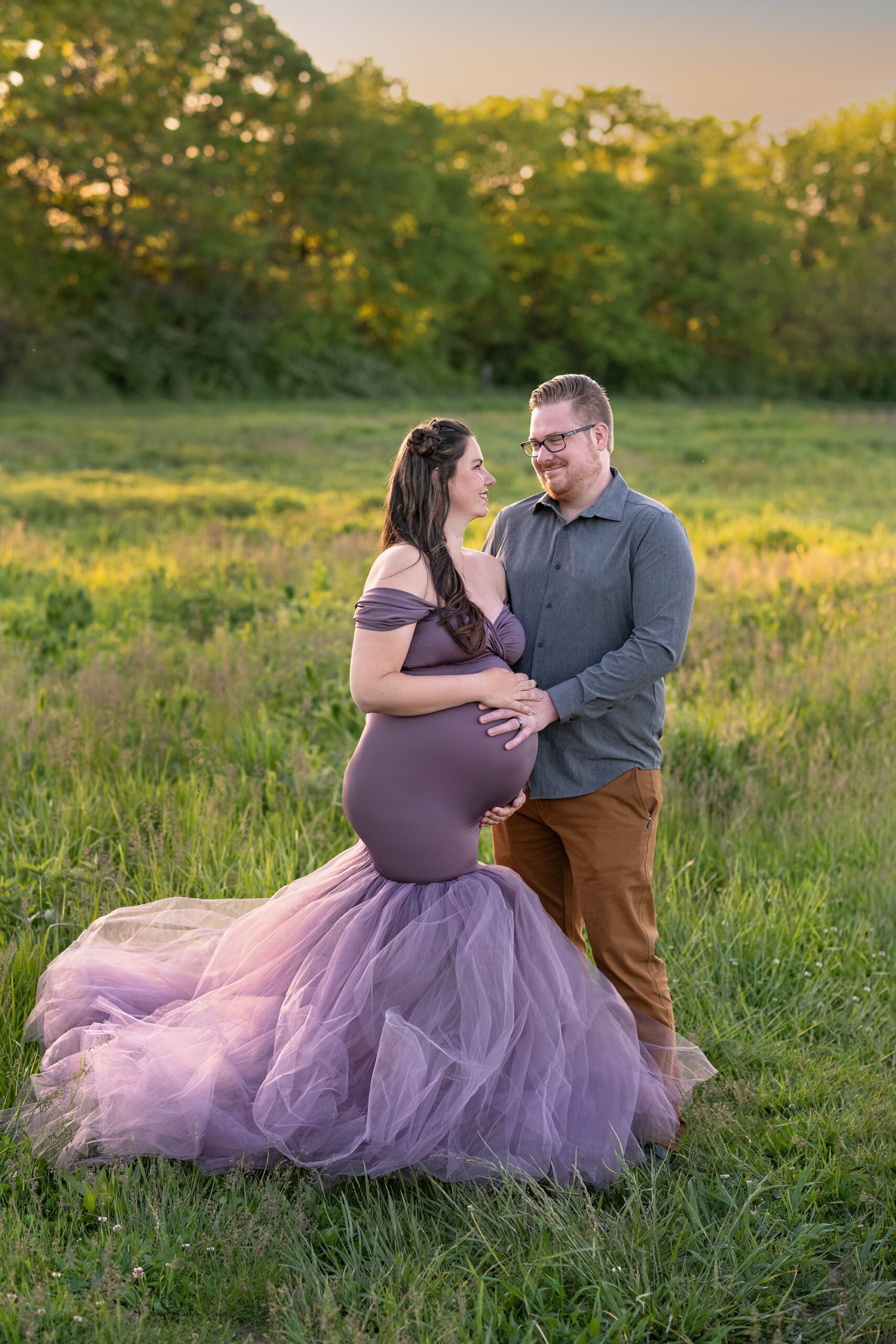 Couple posing at an outdoor maternity photoshoot. They are looking at each other, and each have a hand on mom's belly.