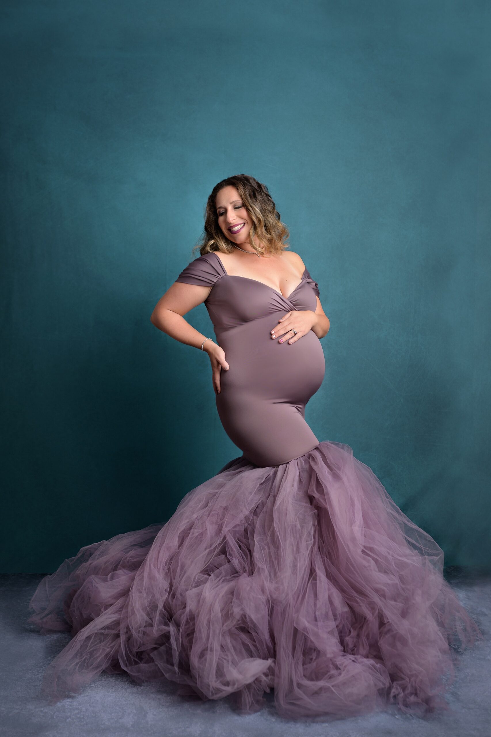 Pregnant mom in a mermaid style purple gown, posing in a Kansas City studio during her maternity session with Helen Ransom.