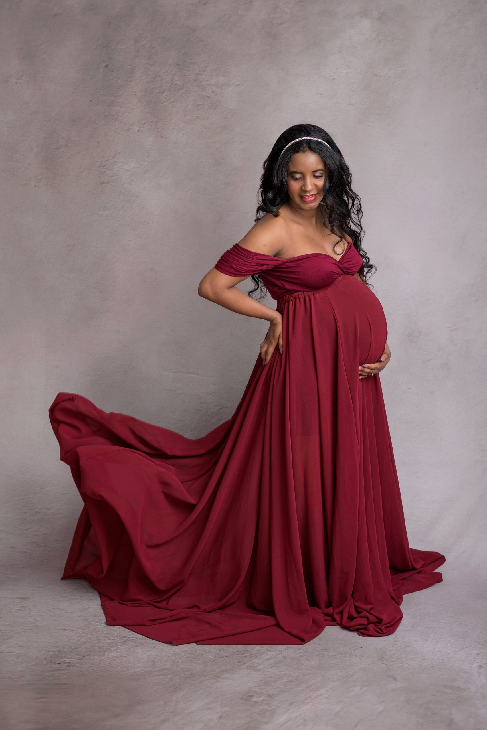 Pregnant mom in a maroon dress with the train floating in the air behind her.