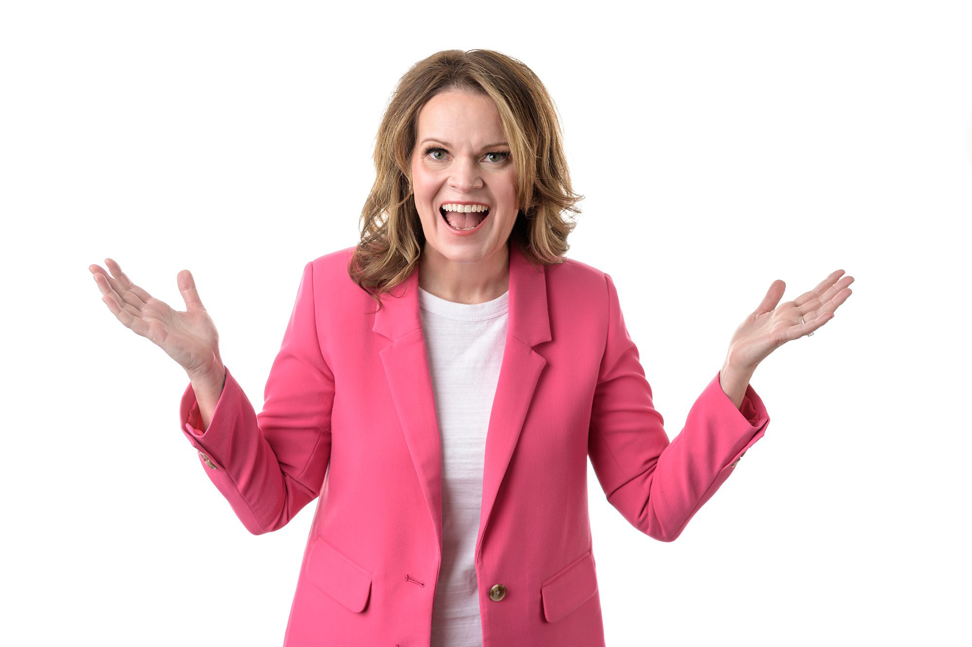 Woman in a white tee shirt and pink blazer, with her hands up and an excited expression on her face.