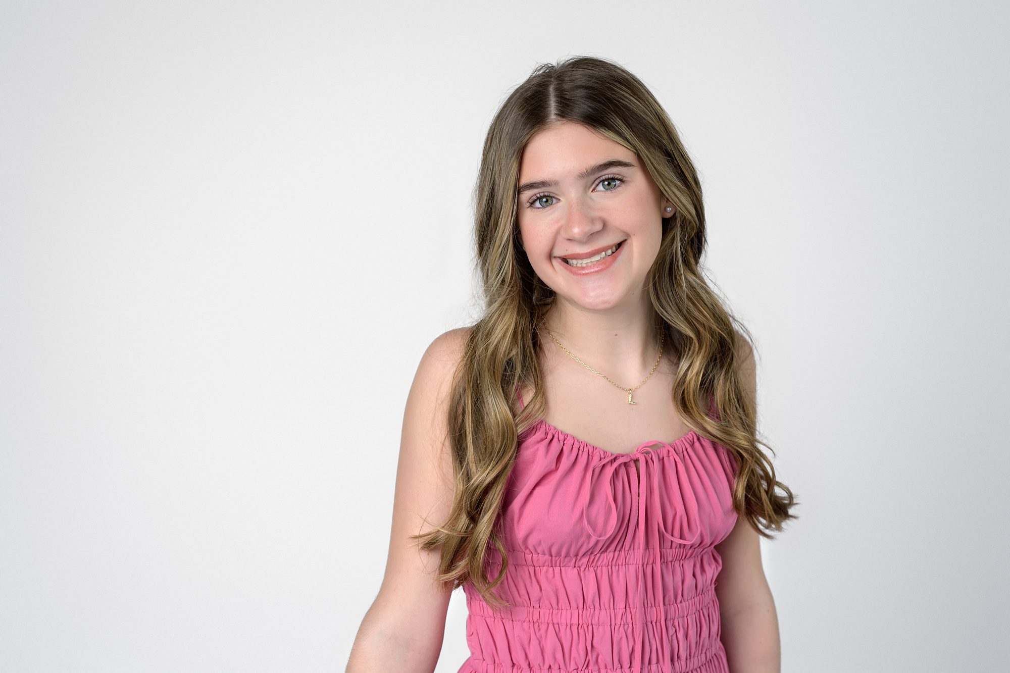 Teen girl with long brown hair in a pink dress, on a white background. Photo is a close-up taken at their family picture session in Overland Park.