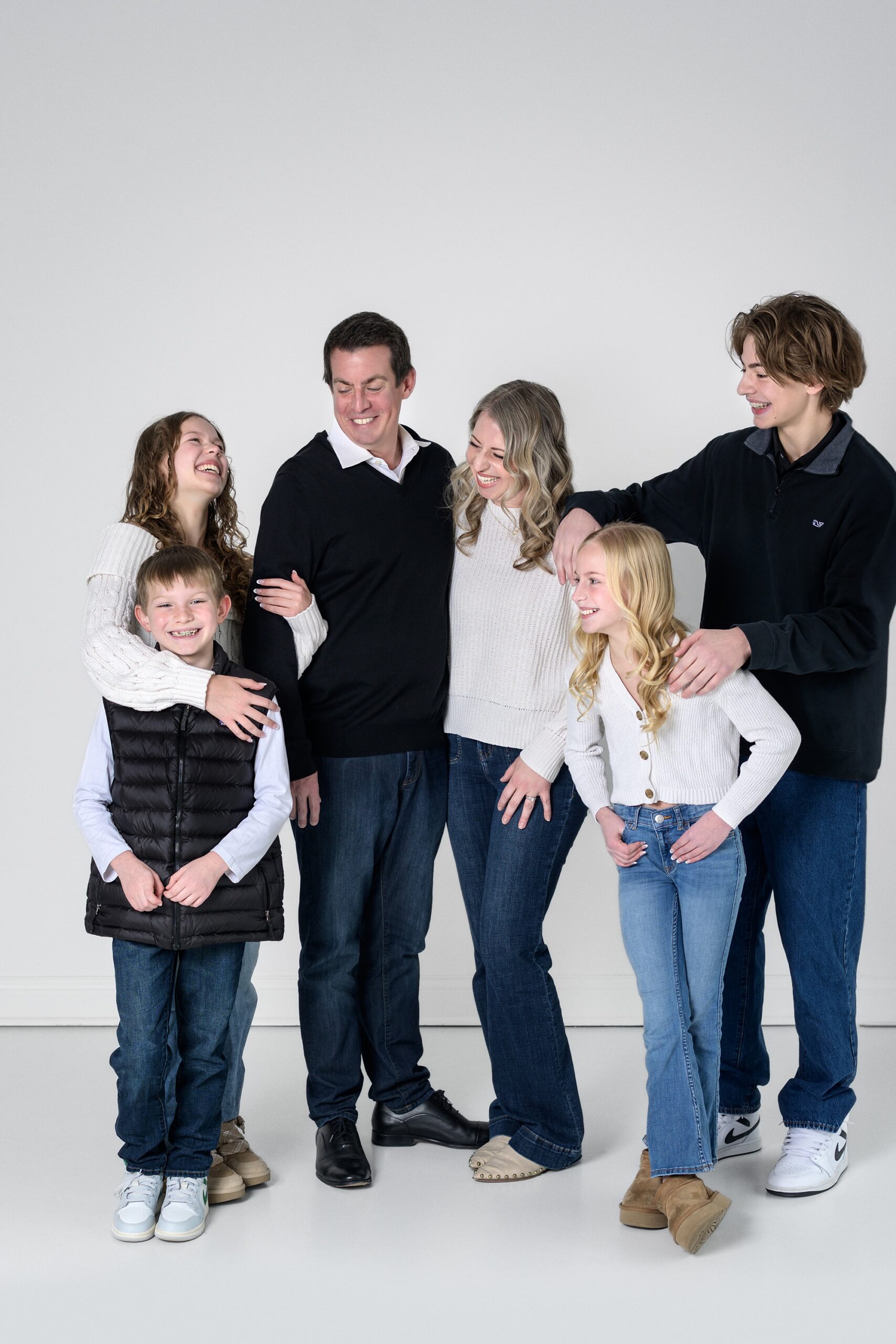 Family of 6, all dressed in black and white, standing and laughing together in a fun photo studio picture in Overland Park.