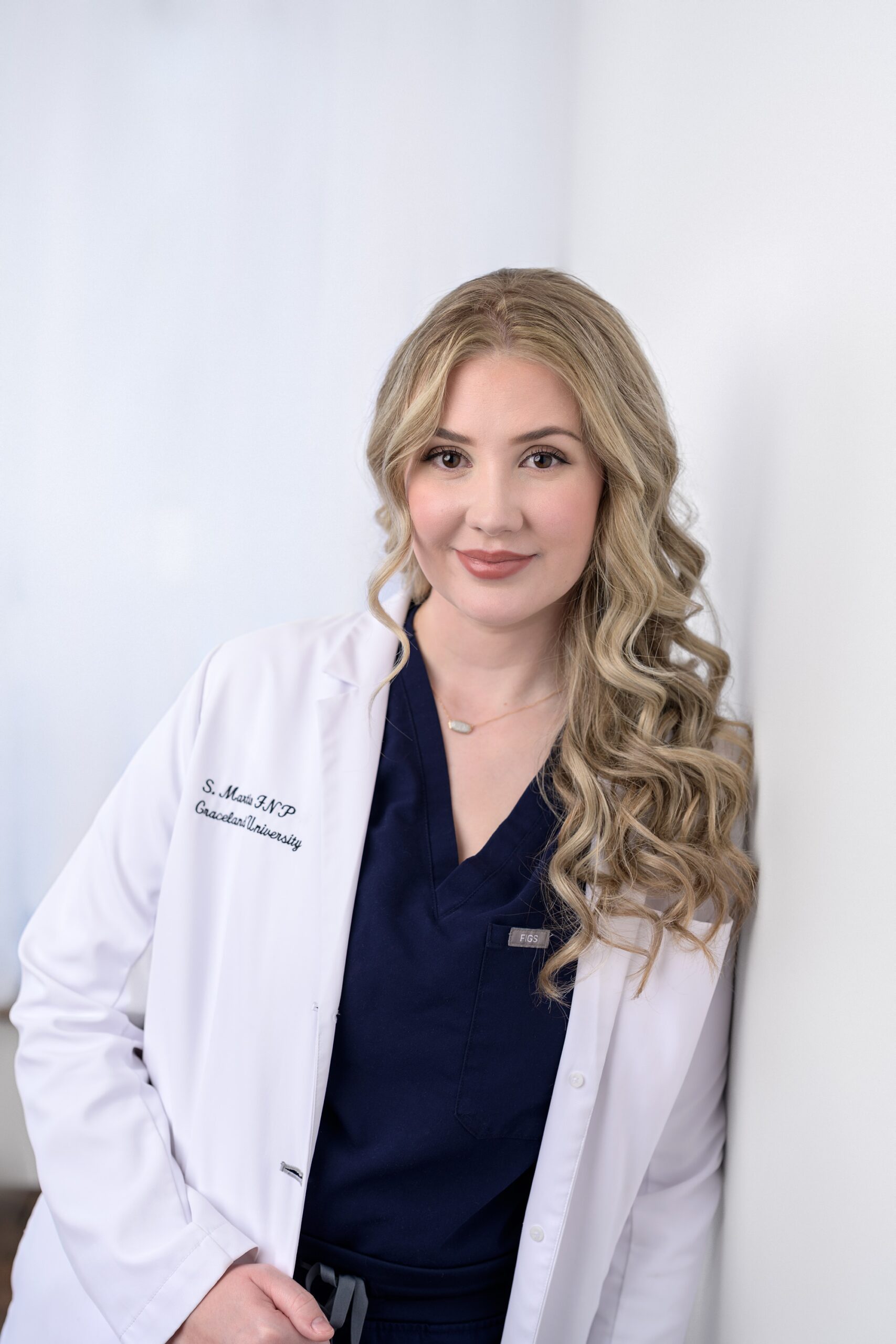 Medical professional posing for a headshot in her scrubs and white jacket.