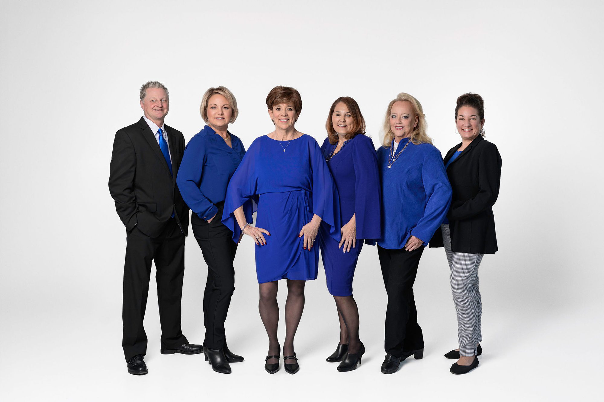 Team of Realtors posing together for a team picture at their headshot session in Kansas City. They 5 women and one man are all wearing royal blues and black, to match their company branding colors.