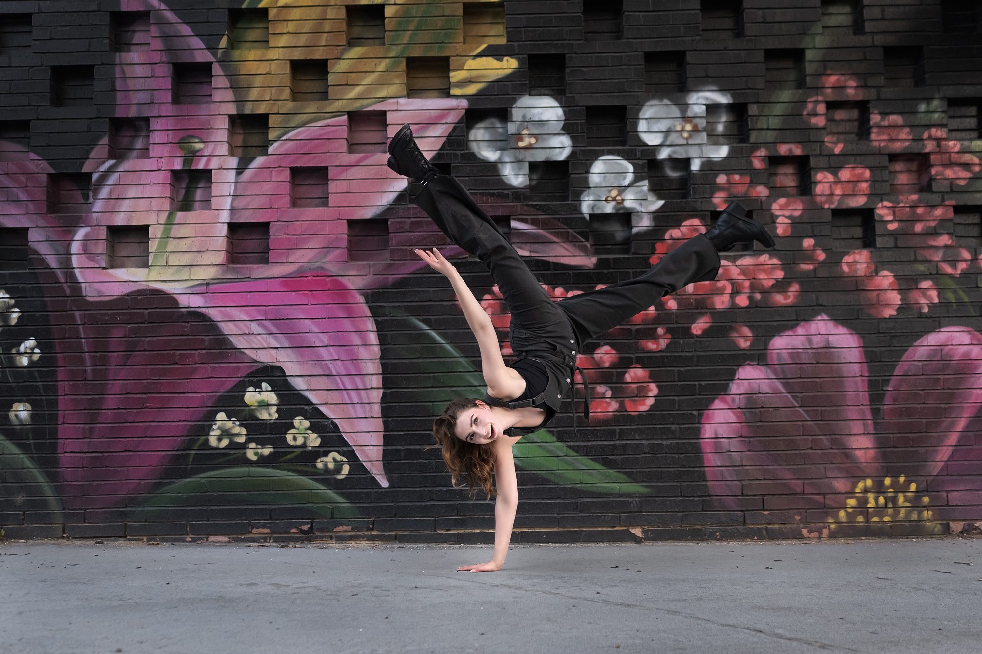 High school girl doing a one armed handstand, in front of a large painted mural, during her senior session in Kansas City with Helen Ransom Photography.